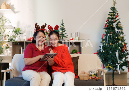 Christmas Cheer. Two women enjoying festive moments with a tablet and decorations in a cozy living room. 133671861