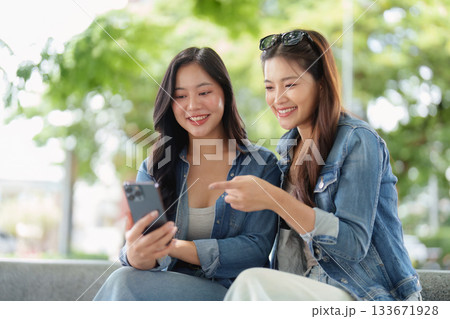 Friendship and Connection. Two young women enjoying a moment together while using a smartphone outdoors. 133671928
