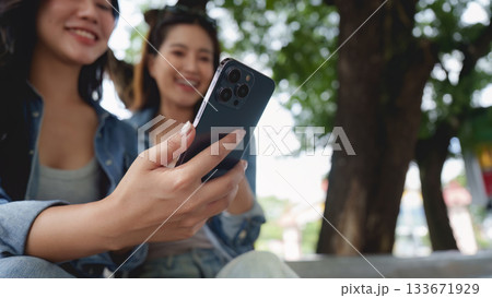 Friendship and Connection. Two young women enjoying a moment together while using a smartphone outdoors. 133671929