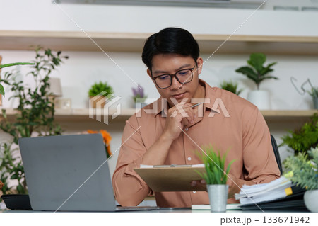 Thoughtful Professional. Man reviewing notes in modern workspace. Thoughtful Professional. Man reviewing notes in modern workspace. 133671942