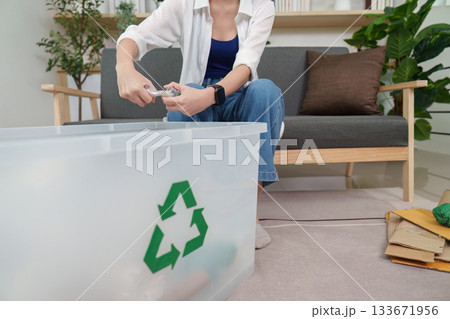 Sustainability. Woman organizing recyclables in a clear bin at home. 133671956