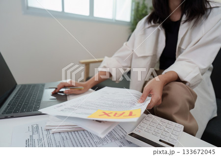 Tax Management. Individual sorting tax papers with calculator and laptop. 133672045