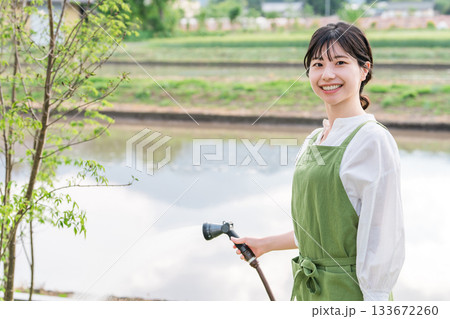 マイホームの庭木に水やりをするエプロン姿のアジア人女性 133672260