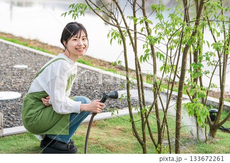 マイホームの庭木に水やりをするエプロン姿のアジア人女性 133672261