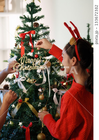 Christmas Spirit. Young girl decorating a festive tree with ornaments and a joyful message. 133672382