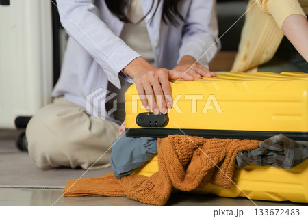 Travel Planning. Friends struggling to close an overstuffed yellow suitcase for their trip. Travel Planning. Friends struggling to close an overstuffed yellow suitcase for their trip. 133672483