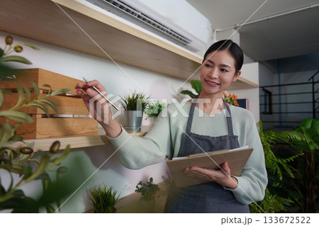 Plant Care. Woman smiling while recording details in a plant shop, promoting sustainability. 133672522