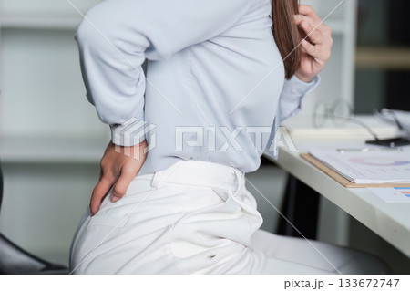 Physical discomfort. Young woman experiencing back pain while working. Physical discomfort. Young woman experiencing back pain while working. 133672747
