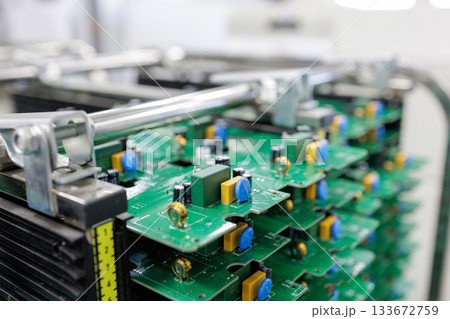 Close view of assembled green printed circuit boards stacked in rack inside modern automated electronics manufacturing plant Close view of assembled green printed circuit boards stacked in rack inside modern automated electronics manufacturing plant 133672759