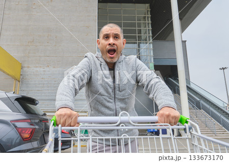 Man opening mouth shouting pushing shopping cart with surprise Man opening mouth shouting pushing shopping cart with surprise 133673170
