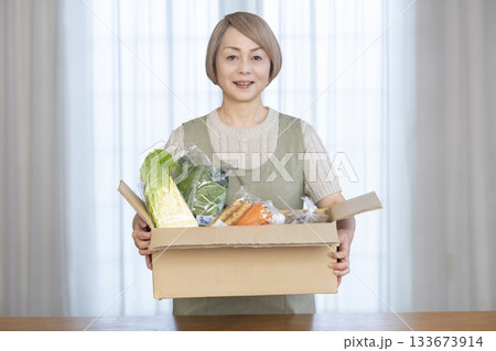 リビングで産地直葬の宅配野菜を喜ぶシニア女性 133673914