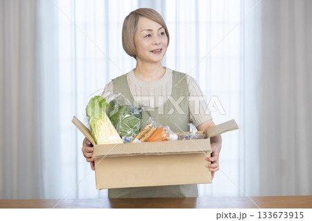 リビングで産地直葬の宅配野菜を喜ぶシニア女性 133673915