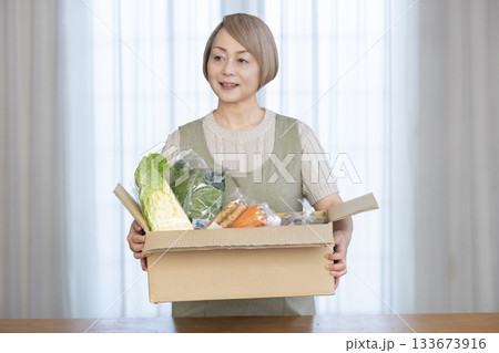 リビングで産地直葬の宅配野菜を喜ぶシニア女性 133673916
