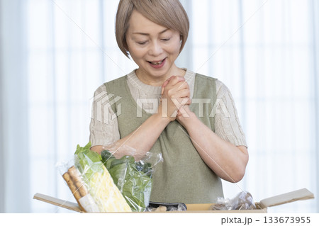 リビングで産地直葬の宅配野菜を喜ぶシニア女性 133673955