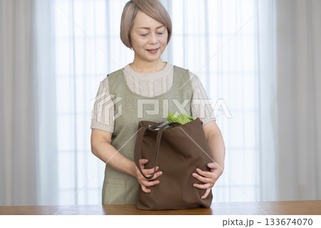 リビングでショッピングバックから野菜を取り出すシニア女性 133674070