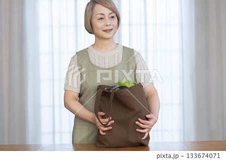 リビングでショッピングバックから野菜を取り出すシニア女性 133674071