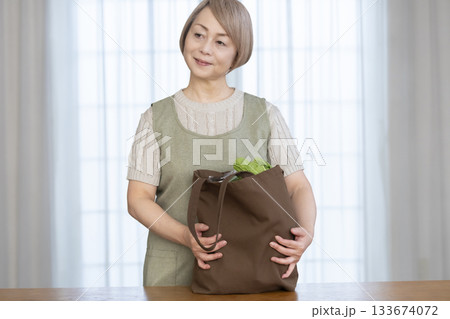 リビングでショッピングバックから野菜を取り出すシニア女性 133674072