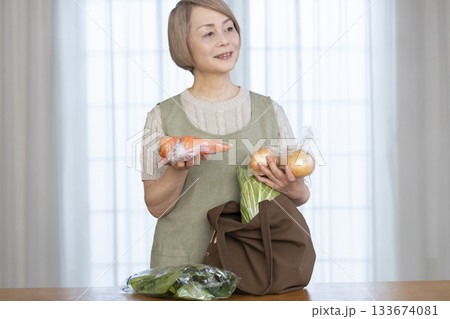 リビングでショッピングバックから野菜を取り出すシニア女性 133674081