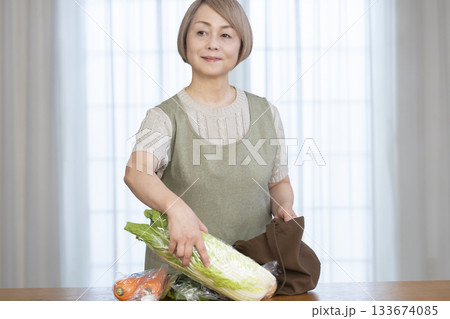 リビングでショッピングバックから野菜を取り出すシニア女性 133674085