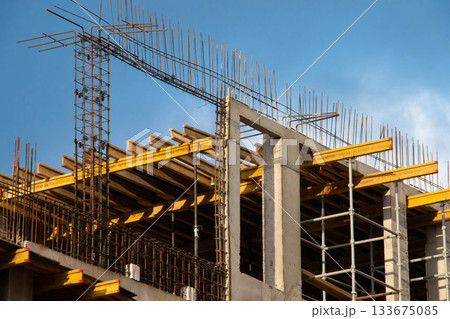 Monolithic Box under Construction with Yellow Volumetric I-Beams. Concrete Wall Frame Building with Formwork Prints and Rebar releases on Construction Site. Architectural origin Structure Sunny day. Monolithic Box under Construction with Yellow Volumetric I-Beams. Concrete Wall Frame Building with Formwork Prints and Rebar releases on Construction Site. Architectural origin Structure Sunny day. 133675085