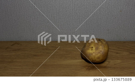 A single potato resting on a wooden surface. 133675889