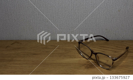 Elegant eyeglasses resting on a wooden table against a textured wall. 133675927