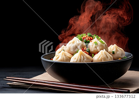 Steam Rising from Delicious Dumplings in a Black Bowl with Scallions and Cooked Sauce 133677312