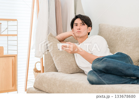 ソファーに寝そべってスマホを見ながらくつろぐ若いアジア人男性 133678680
