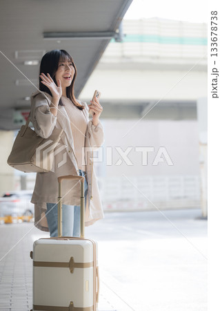 空港や交通機関のターミナルででスマホを持つ女性の写真 旅行や休日のイメージ横顔全身で手を振る 空港や交通機関のターミナルででスマホを持つ女性の写真 旅行や休日のイメージ横顔全身で手を振る 133678738