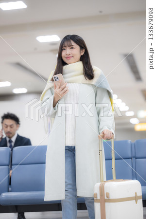 冬の空港ロビーでスマホとスーツケースを持つ若い女性の旅行シーン 冬の空港ロビーでスマホとスーツケースを持つ若い女性の旅行シーン 133679098