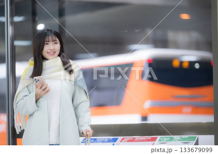 冬の年末年始の帰省、駅のホームやバスターミナルなどでスマホを持つかわいいストールを巻いた女性 133679099