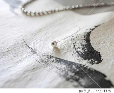 手漉き和紙に滲む墨跡とシルバーアクセサリーの対比──高級感と静寂を兼ね備えた洗練ジュエリー構図 133681129