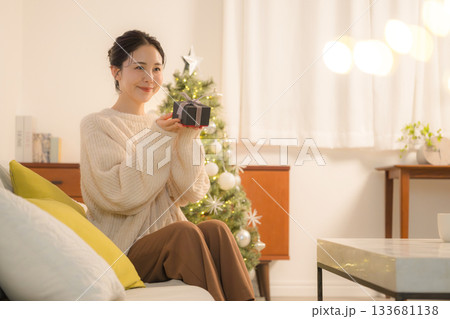 クリスマスツリー前でプレゼントを手に微笑む女性の贈り物シーンと冬のホリデーイメージ 133681138