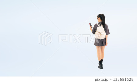スマホを見ながら歩く10代の女性の後ろ姿の全身写真 スマホを見ながら歩く10代の女性の後ろ姿の全身写真 133681529