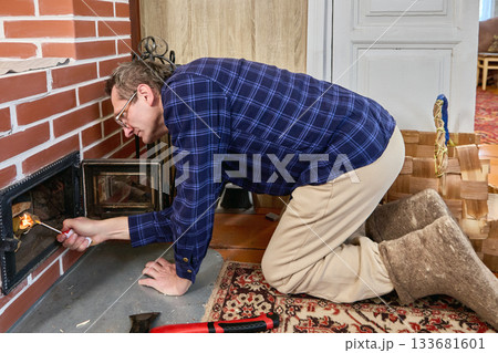 Lighting fire in wood brick stove, middle aged man uses gas lighter, kneeling in front of stove opening. Lighting fire in wood brick stove, middle aged man uses gas lighter, kneeling in front of stove opening. 133681601