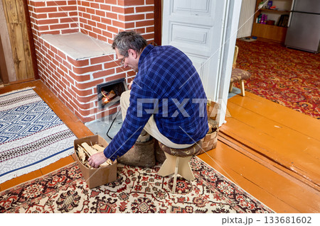 Mature man lights wood stove in country house. 133681602