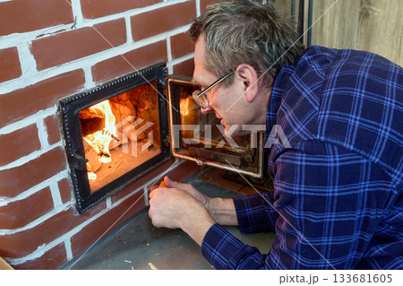 Wood stove heating country house middle aged man maintains fire brick wood burning stove. Wood stove heating country house middle aged man maintains fire brick wood burning stove. 133681605