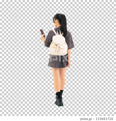 A teenage girl walking while looking at her smartphone. A hand-cut, transparent, full-body PNG photo. 133681720