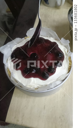 Blueberry sauce spooned over whipped cream cheesecake with graham crust, enticing dessert presentation and glossy berry topping 133681802
