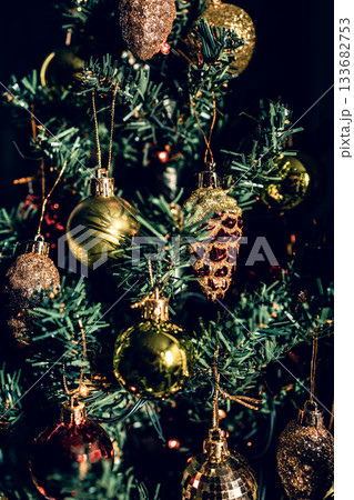 The green Christmas tree is decorated with gold baubles and glittering ornaments, creating vibrant reflections and a winter holiday atmosphere. The green Christmas tree is decorated with gold baubles and glittering ornaments, creating vibrant reflections and a winter holiday atmosphere. 133682753