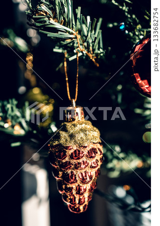The green Christmas tree is decorated with gold baubles and glittering ornaments, creating vibrant reflections and a winter holiday atmosphere. 133682754