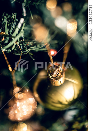 The green Christmas tree is decorated with gold baubles and glittering ornaments, creating vibrant reflections and a winter holiday atmosphere. 133682755