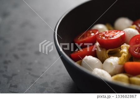 fettuccine pasta with pesto, mozzarella and cherry tomatoes in black bowl on concrete background closeup with copy space 133682867