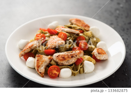 fettuccine with pesto, tomatoes , mozzarella and chicken on white plate fettuccine with pesto, tomatoes , mozzarella and chicken on white plate 133682875