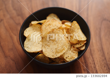 Organic potato chips with black pepper in black ceramic bowl on walnut wood background Organic potato chips with black pepper in black ceramic bowl on walnut wood background 133682894