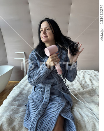 Woman Drying Hair With Compact Pink Hair Dryer at Home, Daily Beauty Routine in Cozy Bathrobe	 133683274