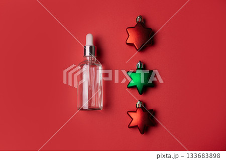 Cosmetic serum on red background with red and green star shaped Christmas ornaments 133683898