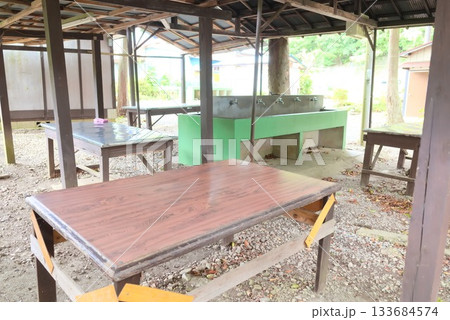 キャンプ場の炊事棟と作業テーブルが並ぶ屋外キッチンスペース 133684574