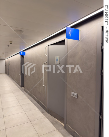 Grey interior of shopping center corridor with public restrooms for men and women, with blue signs on wall. WC entrance features gender symbols. Door to restrooms is separate for men and women 133684712