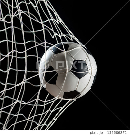 Soccer ball hitting the net during a game with dramatic lighting and classic black and white colors 133686272